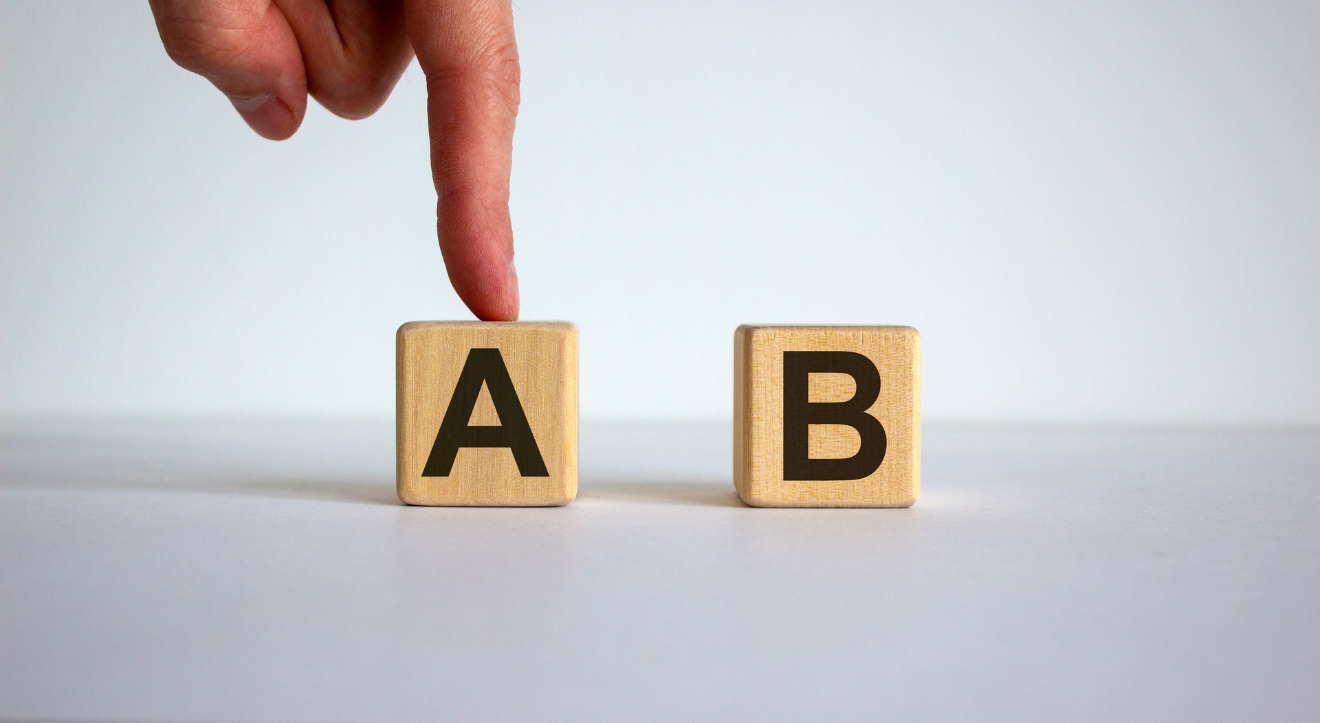 Hand making a choice between two cubes with leteres A and B on neutral background.